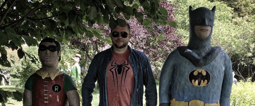 Foto av Per Axbom stående mellan Batman och Robin-statyer i papier-maché. Per har en t-shirt med Spiderman-symbol.