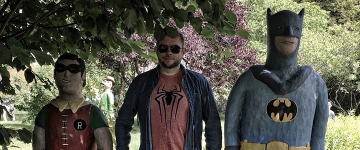 Foto av Per Axbom stående mellan Batman och Robin-statyer i papier-maché. Per har en t-shirt med Spiderman-symbol.